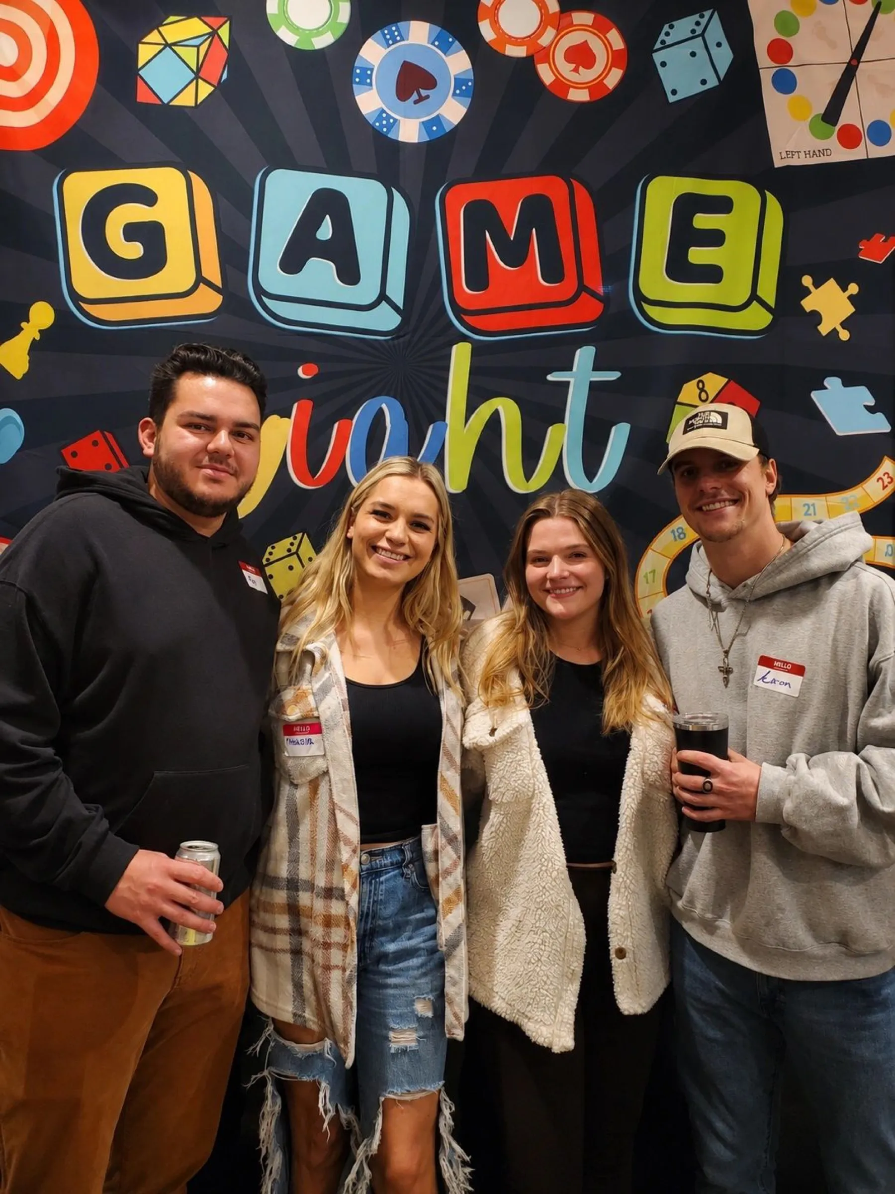 Four friends posing in front of the Game Night backdrop.