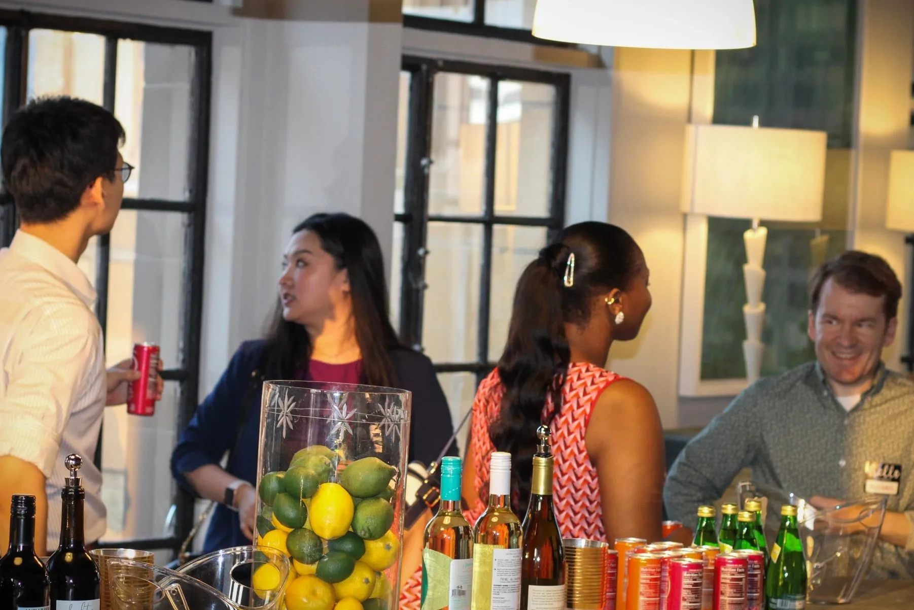 Members chatting around a kitchen island stocked with drinks.
