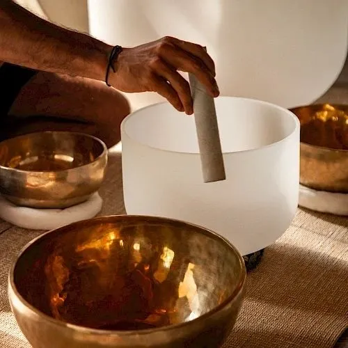 Hands striking a crystal singing bowl beside brass bowls.