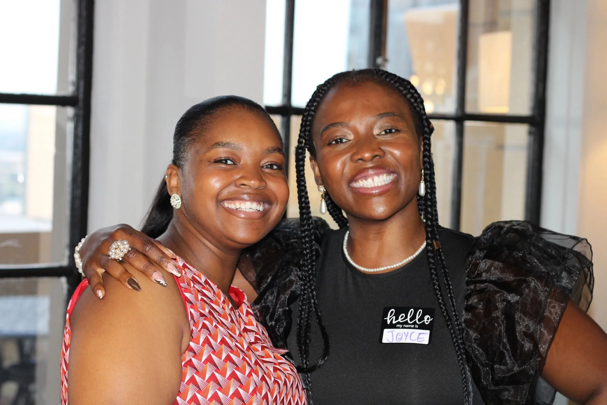 Two women in name tags smiling with their arms around each other.